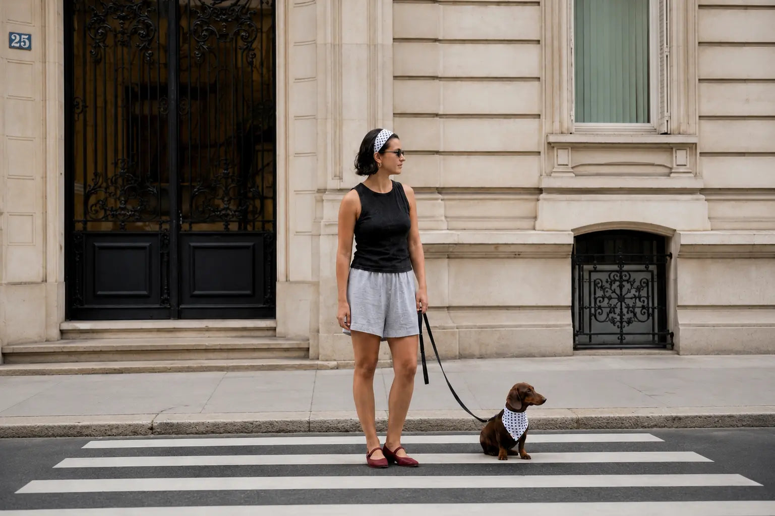 Femme portant un bandeau blanc à pois noirs et teckel chocolat avec un bandana assorti Cocoon Pets traversant une rue de Paris.